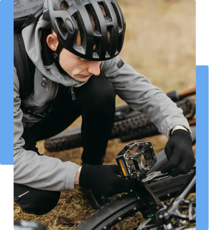 Cyclist in helmet and gloves repairing a bicycle pedal on a grassy trail