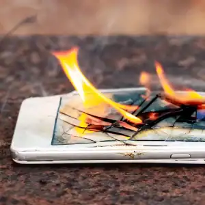 Burning smartphone with cracked screen, representing battery fire hazard in consumer electronics