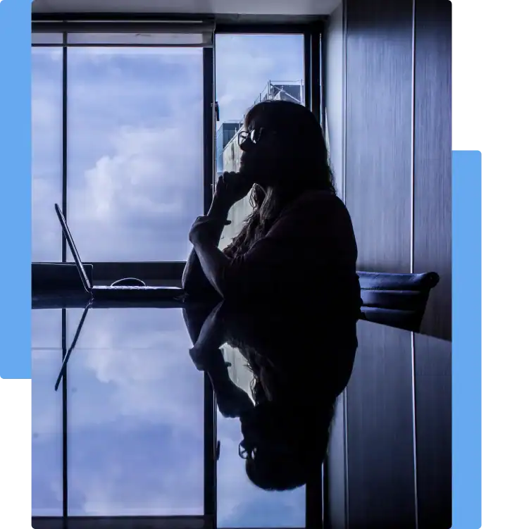 Silhouetted woman sitting at a desk with a laptop, gazing out the window in thought, symbolizing workplace uncertainty or employment legal concerns