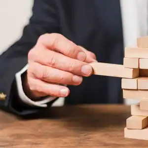 Businessman removing a block from a precarious tower, symbolizing legal and policy risks