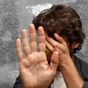 Man shielding his face in fear, suggesting trauma and mistreatment in detention facilities