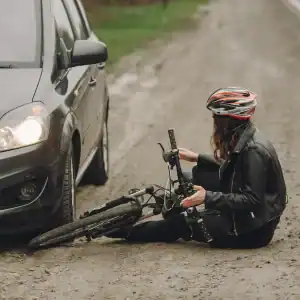 Female cyclist sitting injured on a dirt road after a collision with a vehicle