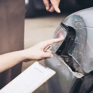 Insurance adjuster examining vehicle damage and taking notes after a crash