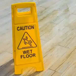 Yellow caution sign on a wet wooden floor indicating slippery conditions