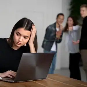 Female employee feeling isolated while coworkers gossip and point behind her