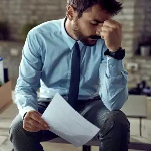 Frustrated man in professional attire sitting with a termination notice in hand