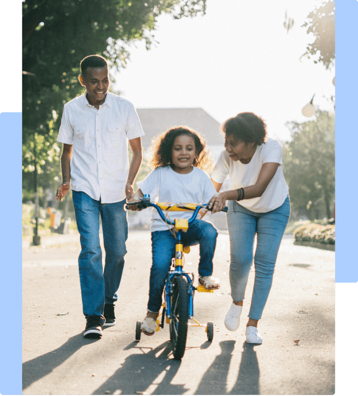 A happy African American family teaching their daughter to ride a bike together on a sunny day.